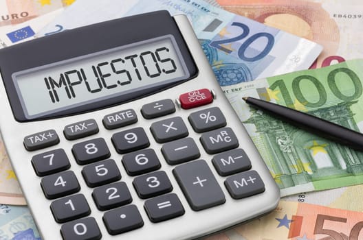 Calculator with money and a pen - Taxes in spanish