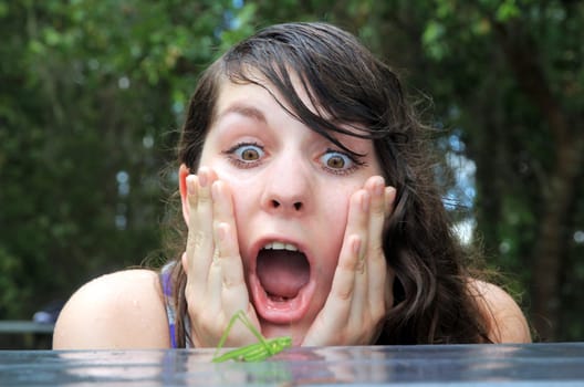 Funny shot of a young woman who is frightened by a grasshopper