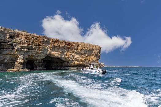 Polignano a Mare, Italy, Apulia - May 24, 2024: View from the water of picturesque cliffs by Adriatic Sea. Tourists sail by boat into a cave in the rocks