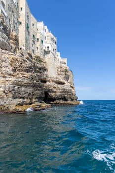 Buildings built on cliffs, view from the sea of ​​picturesque rocks and caves, Polignano a Mare, Italy, Apulia. A cruise along the rocky coast is a great tourist attraction