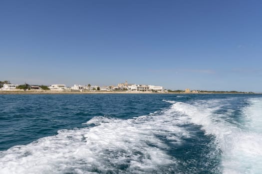 Polignano a Mare, Italy, Apulia - May 24, 2024: Picturesque view from the boat of the Adriatic Sea with a wake and the coast with Abbey of San Vito in the distance