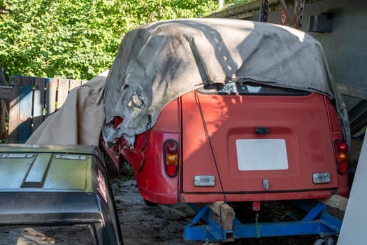 A red car is covered with a tarp and is parked in a garage. The car is old