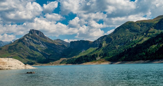A beautiful mountain range with a lake in the foreground. The sky is cloudy, but the sun is shining through the clouds