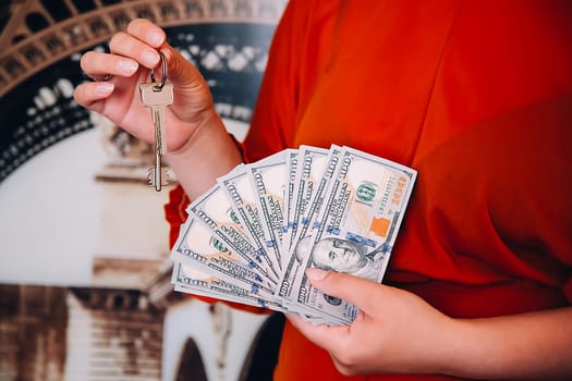 A girl in a red blouse is holding a fan of American dollars and the keys to the apartment.
