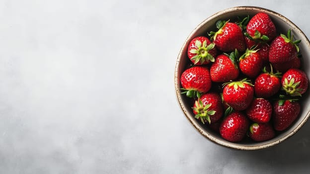 Juicy red strawberries with green leaves in a white ceramic bowl on a light background, offering ample copy space.
