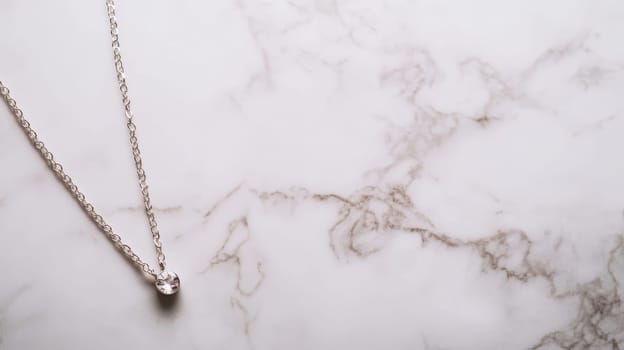 Elegant silver necklace with a small pendant on a white marble background, perfect for jewelry photography or product showcase.