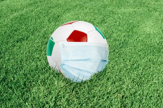 Soccer ball in italian colors with mask on green field. Virus threatened championship concept