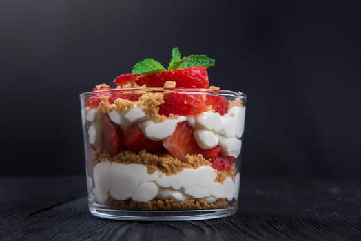 Strawberry with cookie and cream dessert decorated with mint leaf on black wooden background