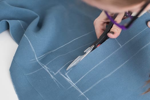 Woman dressmaker cutting fabric textile with scissors