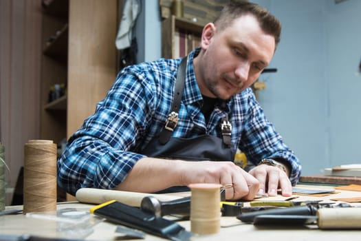 Man working with leather textile at a workshop. Craftman cutting leather. Concept of handmade craft production of leather goods.