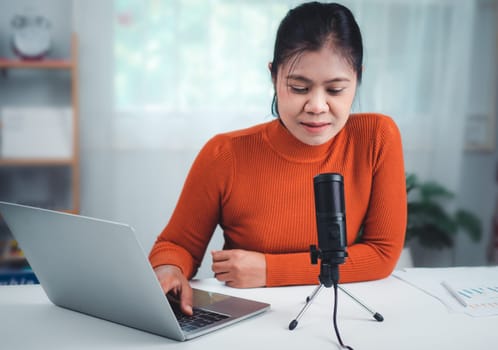 Woman talking into microphone on stand, lead on-line communication, discuss topic, looks at notebook screen, engaged in streaming, virtual meeting event, Podcast, webinar, Content creator concept.