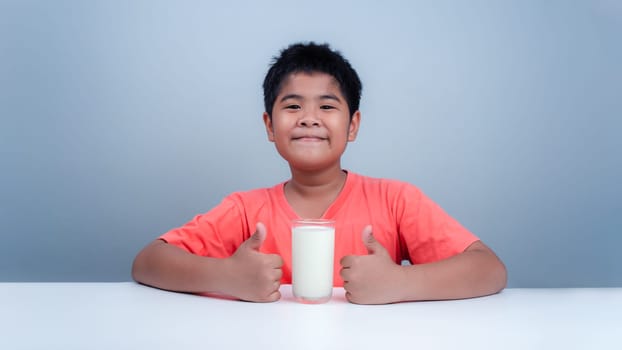 Concept of happy good nutrition, Portrait of a little young handsome kid boy in pink t-shirt, Holding a glass of milk on grey background, Smiling of Asian boy with a glass of milk.