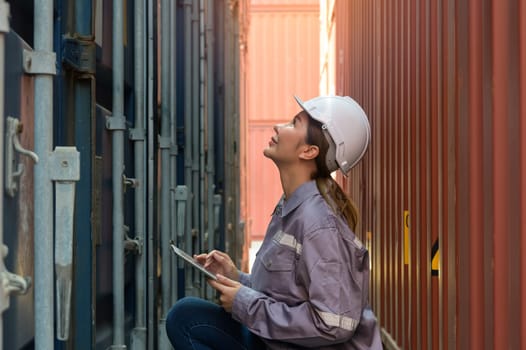 Happiness female engineer working at international shipping cargo yard. Woman in uniform using digital tablet while looking at container for inspection loading information. Transportation and shipping concept