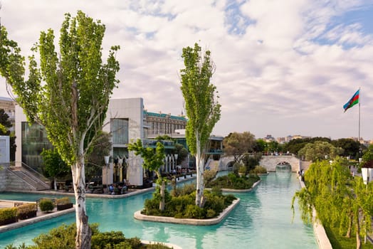 Baku, Azerbaijan - May 4 2024: The Boulevard canals, or Little Venice, surrounded by lush greenery, and Azerbaijani flag in distance