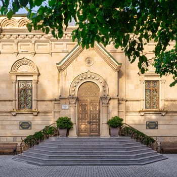 Grand entrance of Holy Myrrhbearers Cathedral in Baku, Azerbaijan, features ornate designs, decorated arched door, lovely stained glass windows, and inviting staircase, surrounded by vibrant greenery