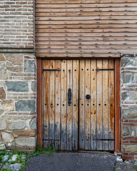 The sturdy wooden door features intricate iron details, set against a weathered stone wall, suggesting a rich history in this quaint area. Lush grass and soft shadows enhance the scene's charm
