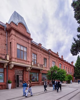 Ganja, Azerbaijan - May 13, 2024: Visitors enjoy a leisurely walk along Javad Khan Street, surrounded by vibrant greenery and unique brick architecture under a cloudy sky