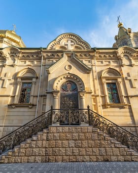 Ornate side entrance of Holy Myrrhbearers Cathedral, in Baku, Azerbaijan, characterized by intricate architecture, decorated metal door, and vibrant stained glass widows