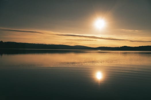 Sunrise over a Swedish lake with mirror-smooth water in front of trees on the shore. Nature shot from Scandinavia