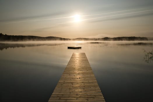 Wooden jetty in the morning in fog, on a Swedish lake. A floating island in the background. Scandinavian nature