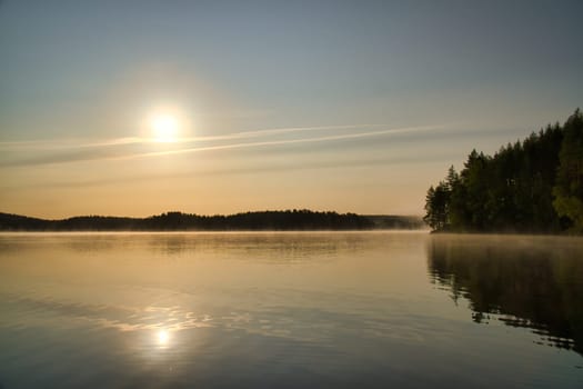 Sunrise over a Swedish lake with mirror-smooth water in front of trees on the shore. Nature shot from Scandinavia