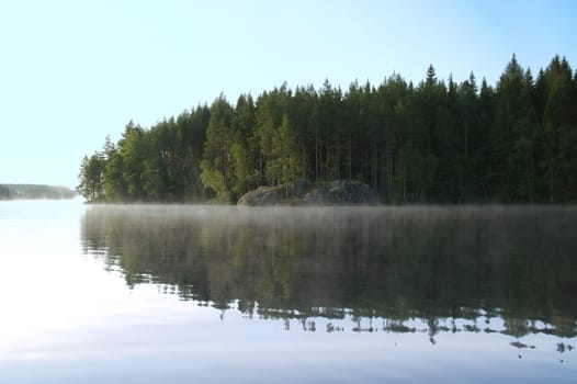 Lake in Sweden at sunrise with romantic light, blue water and trees on the shore. Scandinavian nature in the north