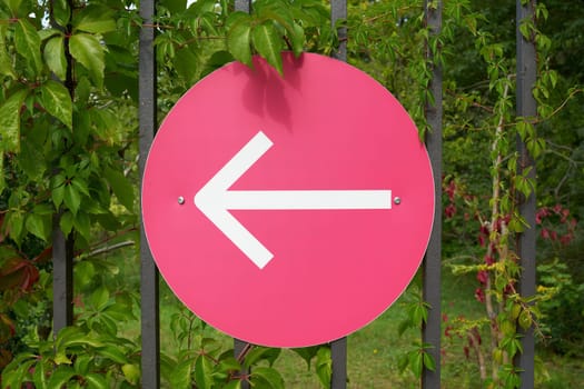 Sign with an arrow pointing left on a fence, indicating the right direction