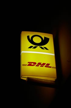 Illuminated sign of a post office of the German logistics company DHL in Berlin in the evening