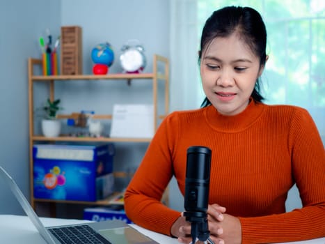 Woman talking into microphone on stand, lead on-line communication, discuss topic, looks at notebook screen, engaged in streaming, virtual meeting event, Podcast, webinar, Content creator concept.