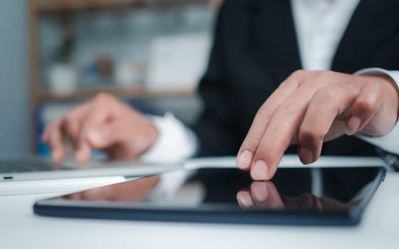 Businesswoman in black suit using digital tablet and working on laptop computer on table at office. Businesswoman finger touching on tablet screen at desk and suring the internet, close up