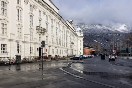 Innsbruck, Austria - February 26, 2023: Hofburg, former Habsburg palace, it is one of three most significant cultural buildings in the country. Peaks of the snowy Alps mountains in the clouds in the distance
