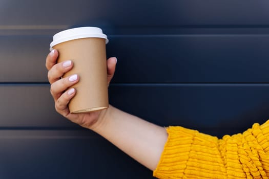 A woman in a bright yellow sweater is seated with her leg crossed, delicately holding a cup of coffee in her hand while gesturing with her other hand