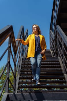 Middle-aged woman descending an outdoor staircase with one hand on the railing.