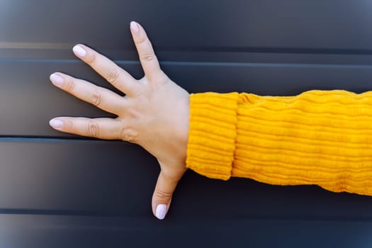 Human hand with spread fingers in yellow sleeve against dark lined backdrop.