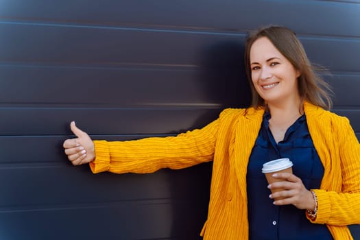 Confident woman giving thumbs-up while holding coffee cup.