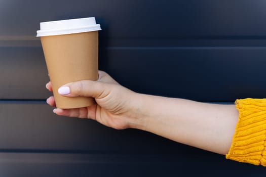 Hand holding disposable coffee cup on blue background.