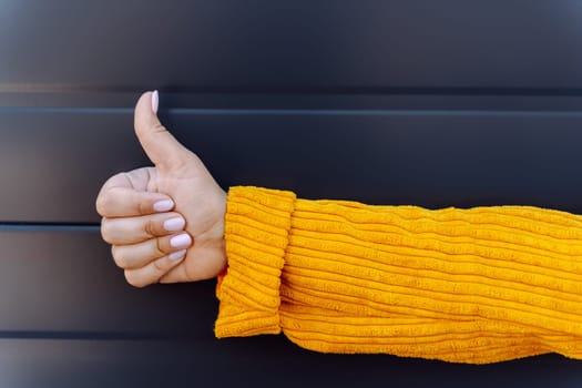 Person giving thumbs up in yellow sweater against dark striped background.