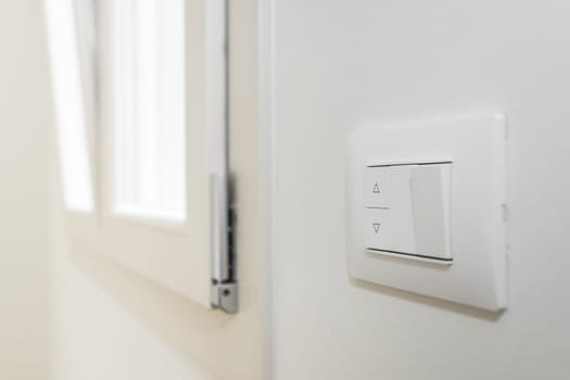 White frame and buttons of the roller shutter switch up and down on white wall in the house