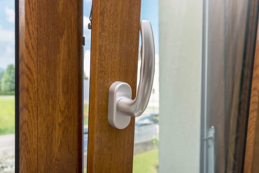 Wooden window open detail. Bottom hung window. Wooden, Metal, PVC door frame closeup view. Stylish chrome handle. Energy efficient and safety profile. Residential garden blurred background.