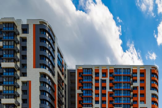 freshly built high rise apartment building on blue sky background with white clouds.