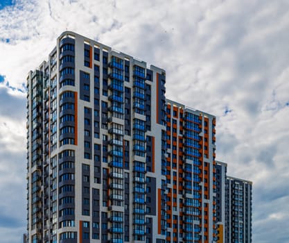 freshly built high rise apartment building on blue sky background with white clouds.