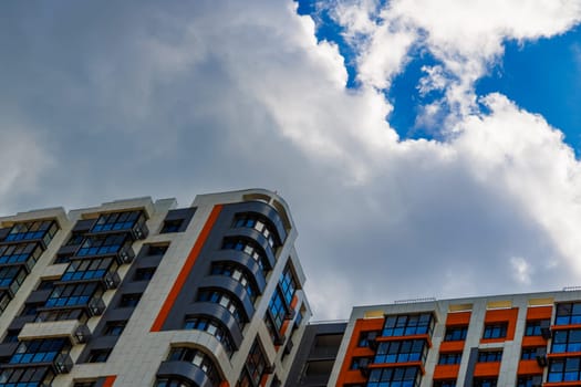 freshly built high rise apartment building on blue sky background with white clouds.
