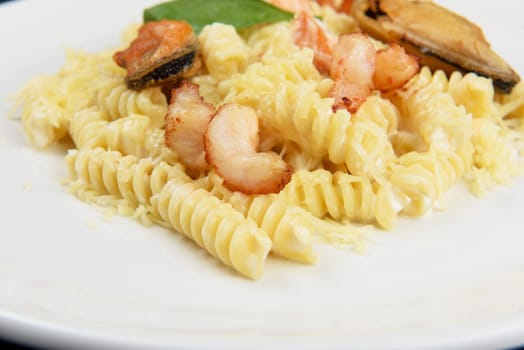 Seafood Pasta with mussels salmon and shrimps with basil in white plate on black wooden background.