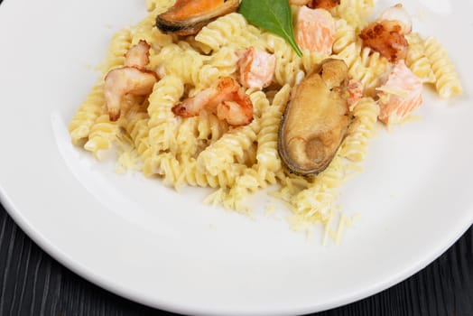 Seafood Pasta with mussels salmon and shrimps with basil in white plate on black wooden background.