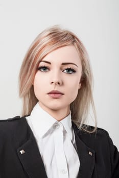 Young businesswoman with striking blue eyes and dyed blonde hair is posing in front of a white background. She is wearing a black jacket and a white shirt
