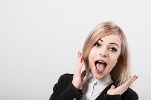 Shocked, excited businesswoman in a suit jacket stands against a white background, exuding joy and amazement with wide eyes and open mouth