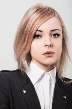 Confident young businesswoman in studio, wearing white shirt and black jacket, exuding determination and ambition. Serious expression reflects leadership and modern style
