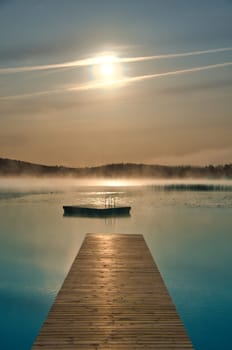 Wooden jetty in the morning in fog, on a Swedish lake. A floating island in the background. Scandinavian nature