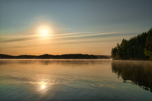 Sunrise over a Swedish lake with mirror-smooth water in front of trees on the shore. Nature shot from Scandinavia