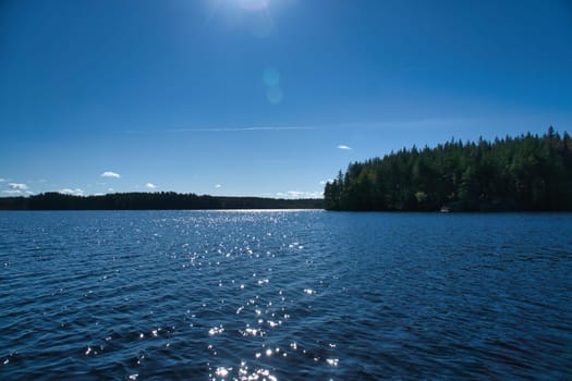 Lake in Sweden with blue sky, blue water and trees on the shore. Scandinavian nature in the north